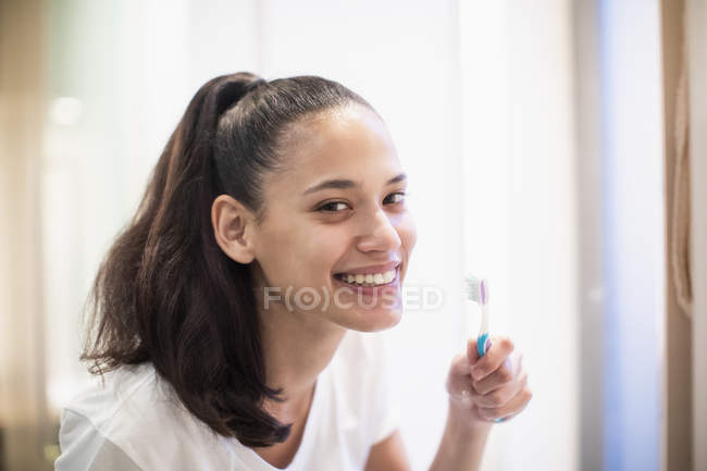 Портрет улыбающейся, уверенной женщины, чистящей зубы в зеркале ванной — стоковое фото