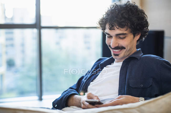 Sorrindo homem usando telefone inteligente no sofá — Fotografia de Stock