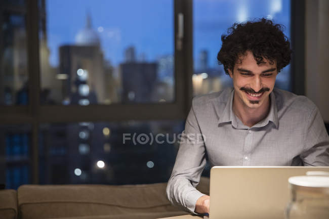 Homem usando laptop em apartamento urbano à noite — Fotografia de Stock