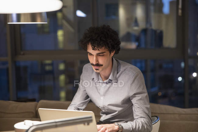 Homem focado trabalhando em laptop em apartamento urbano à noite — Fotografia de Stock