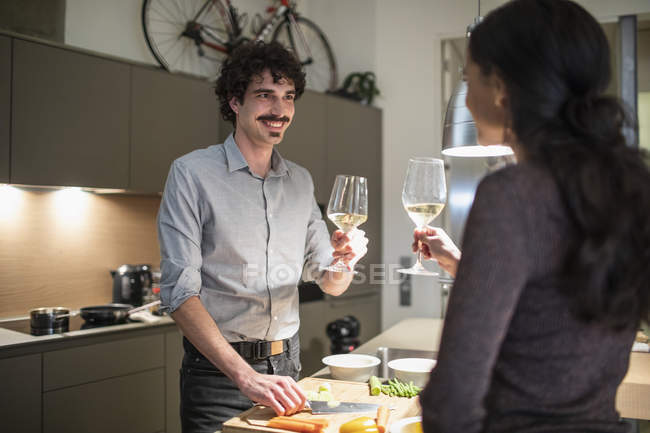 Couple preparing dinner and drinking white wine in apartment kitchen — Stock Photo