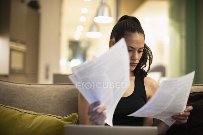 Femme lisant la paperasse à l'ordinateur portable sur le canapé — Photo de stock