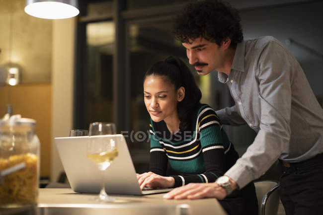 Couple utilisant un ordinateur portable et boire du vin blanc à la maison la nuit — Photo de stock