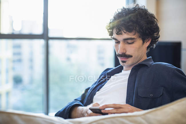 Чоловік використовує смартфон на дивані — стокове фото