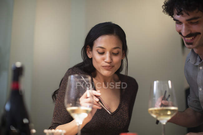 Casal sorridente jantando com pauzinhos e bebendo vinho branco — Fotografia de Stock