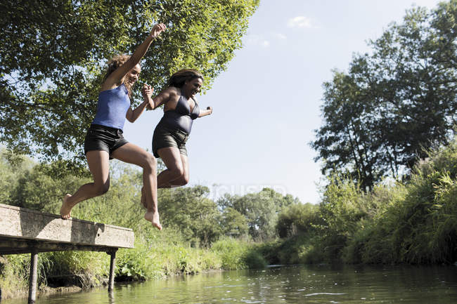 Carefree mother and daughter jumping into river — Stock Photo