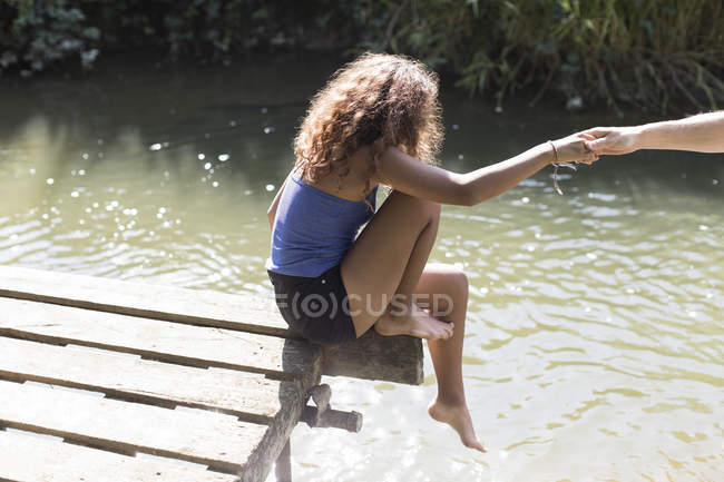 Девушка, сидящая на краю солнечного причала у реки — стоковое фото
