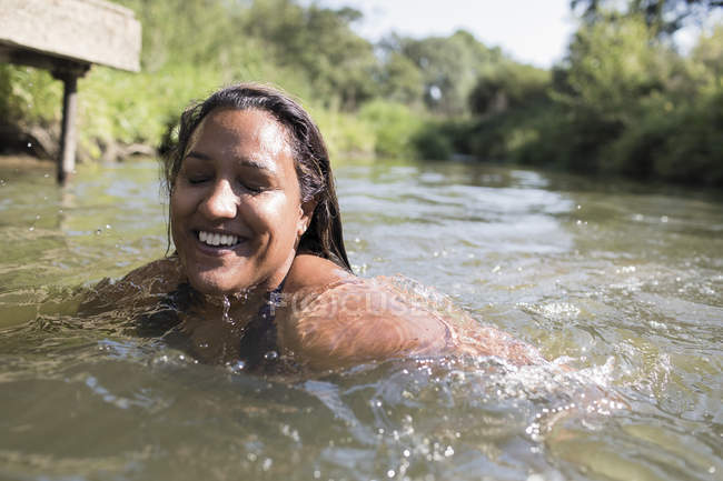 Glückliche, unbeschwerte Frau, die im sonnigen Fluss schwimmt — Stockfoto