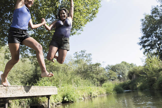 Playful mother and daughter jumping into sunny river — Stock Photo
