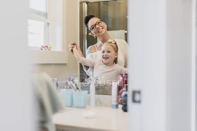 Sorridente madre e figlia nello specchio del bagno — Foto stock