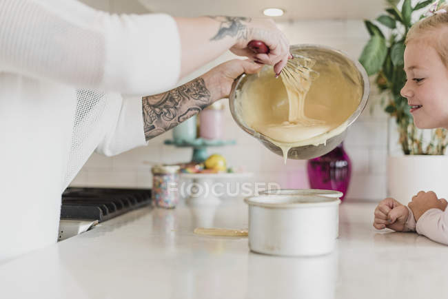 Fille regarder mère avec des tatouages cuisson dans la cuisine — Photo de stock