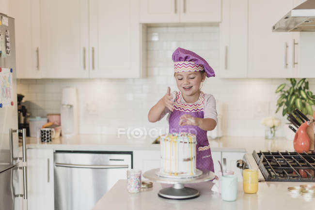 Chica sonriente decorando pastel en la cocina - foto de stock