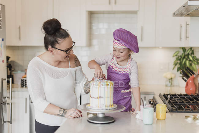 Mother and daughter decorating cake in kitchen — Stock Photo