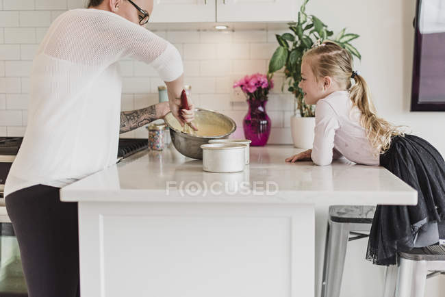 Curioso ragazza guardando madre cottura in cucina — Foto stock