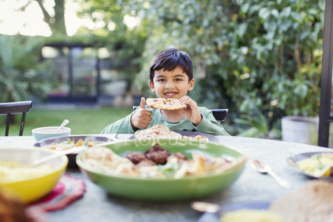 Retrato niño feliz comiendo pan naan en la mesa del patio - foto de stock