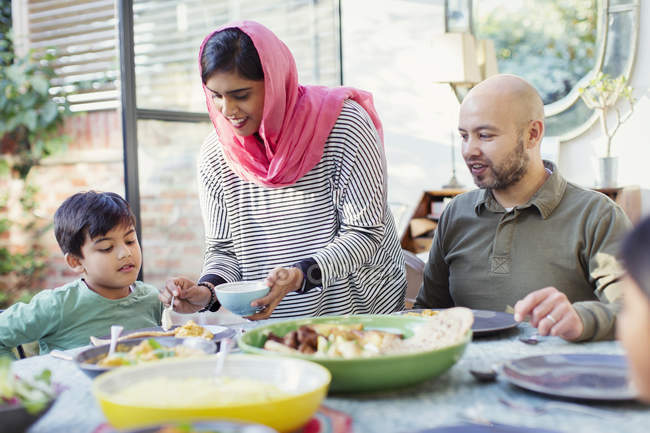 Mother in hijab serving dinner to family at table — Stock Photo