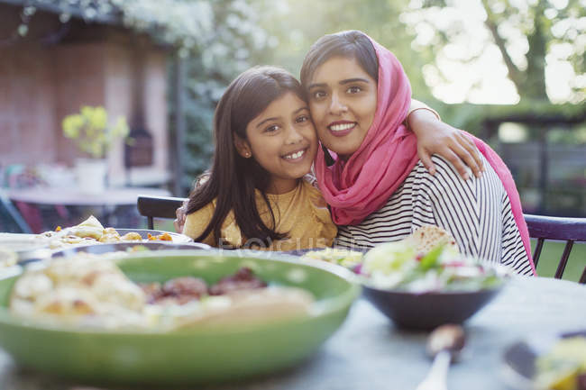 Retrato feliz madre en hijab e hija abrazándose en la mesa de la cena - foto de stock