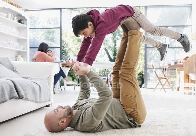 Padre levantamiento hijo con piernas en sala de estar piso - foto de stock