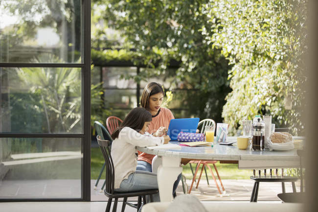Madre e figlia utilizzando il computer portatile e facendo i compiti a tavola — Foto stock