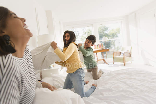 Madre juguetona y niños disfrutando de la pelea de almohadas en la cama - foto de stock