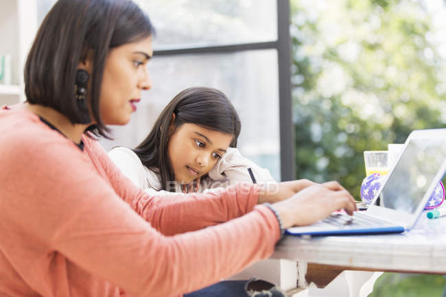 Madre e figlia utilizzando il computer portatile, facendo i compiti a tavola — Foto stock
