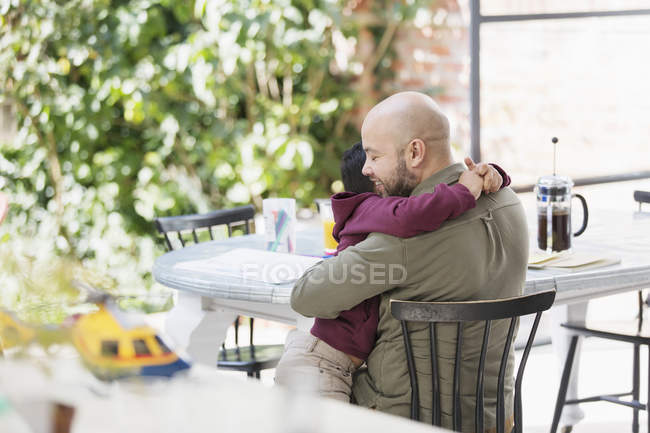 Padre e hijo cariñosos abrazándose en la mesa - foto de stock