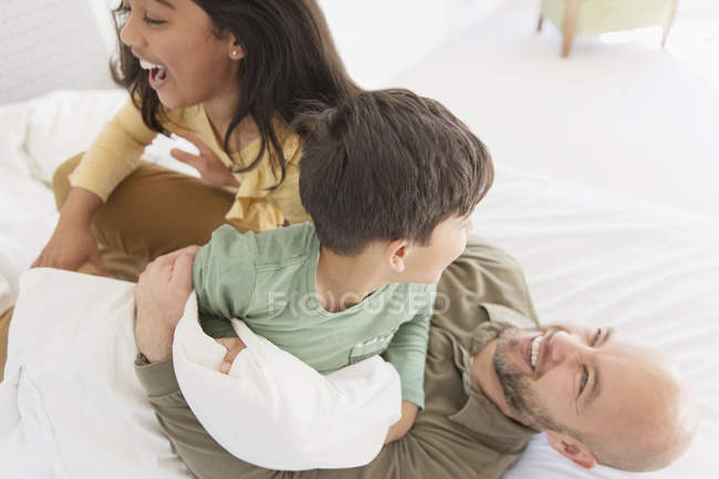 Играющий отец и дети на кровати — стоковое фото