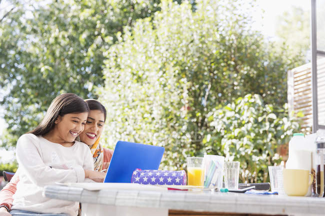 Sonriente madre e hija usando el portátil en la mesa - foto de stock