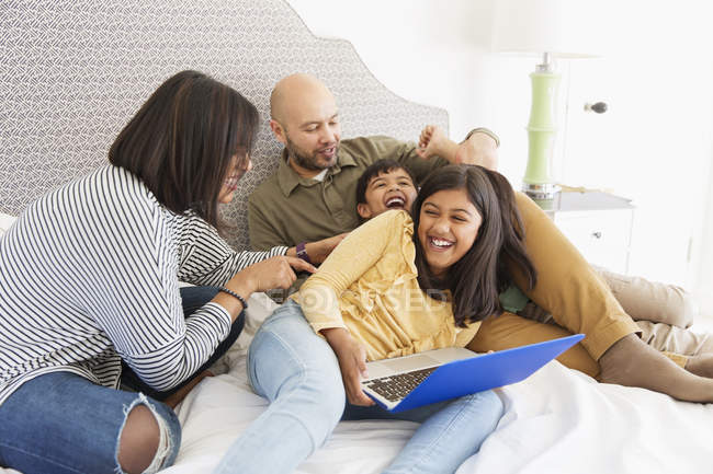 Famiglia giocosa con computer portatile sul letto — Foto stock