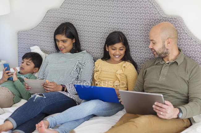 Familia usando tecnología en la cama - foto de stock