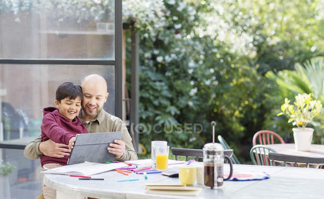 Padre e hijo usando tableta digital en la mesa - foto de stock