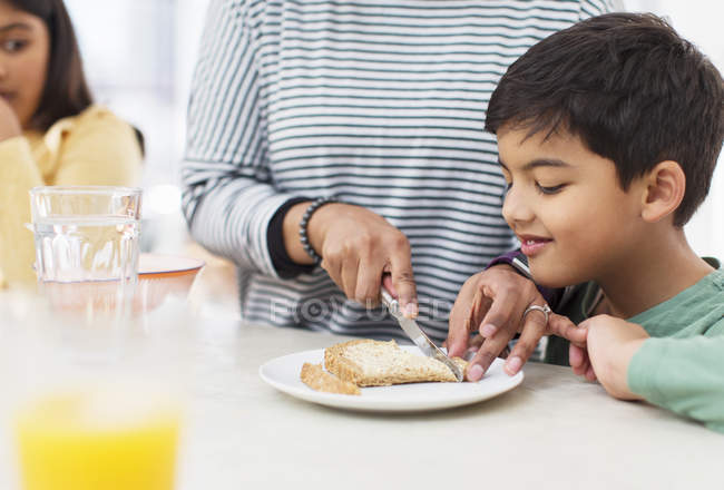 Mother cutting crusts off bread for son — Stock Photo