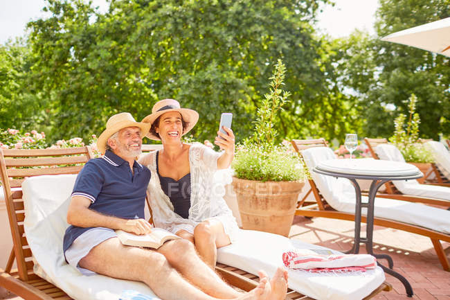 Feliz pareja madura tomando selfie con el teléfono de la cámara en el soleado resort junto a la piscina - foto de stock