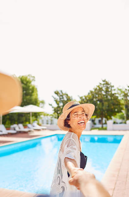 Glückliche Ehefrau führt Ehemann an der Hand am sonnigen Resort-Pool — Stockfoto