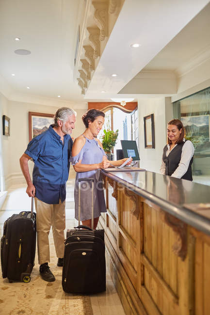 Älteres Paar mit Koffern checkt an Hotelrezeption ein — Stockfoto