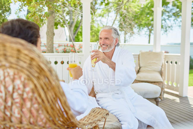 Зрелая пара в гидромассажных халатах пьет мимозы в курортной беседке — стоковое фото
