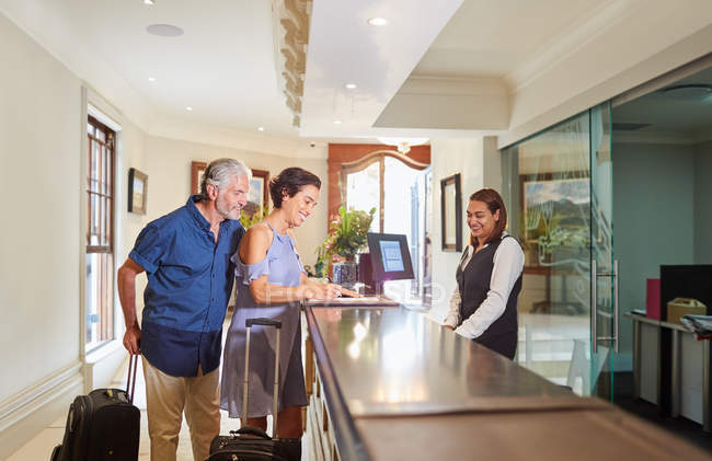 Älteres Paar mit Koffern checkt an Hotelrezeption ein — Stockfoto