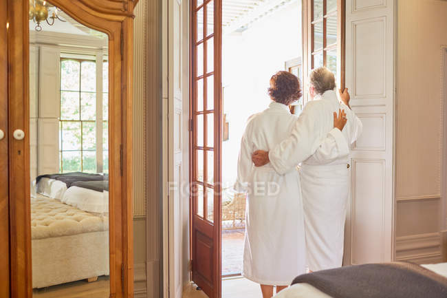 Mature couple in spa bathrobes standing at hotel balcony doorway — Stock Photo
