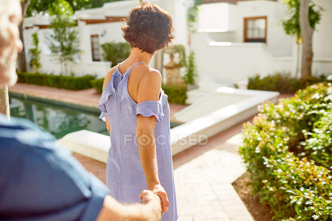 Coppia che si tiene per mano, passeggiando a bordo piscina soleggiata — Foto stock