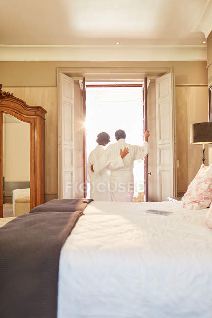 Affectionate couple in spa bathrobes standing at hotel balcony doorway — Stock Photo