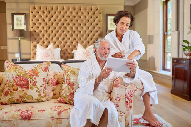 Mature couple in spa bathrobes using digital tablet in hotel room — Stock Photo