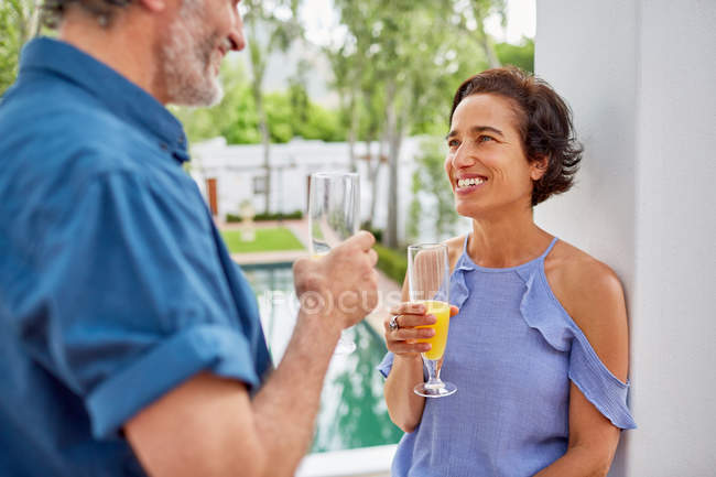 Feliz pareja adulta bebiendo mimosas en el balcón del hotel - foto de stock