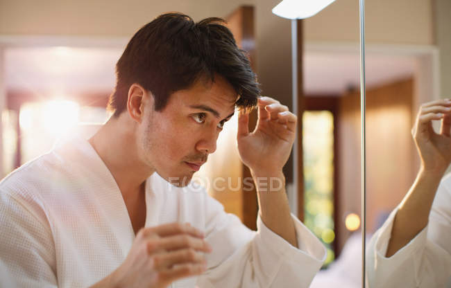 Homme vérifiant les cheveux dans le miroir de salle de bains — Photo de stock