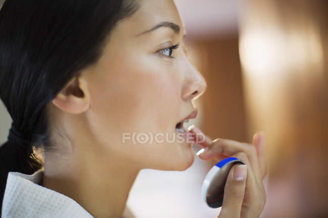 Закройте молодую женщину, применяя бальзам для губ — стоковое фото