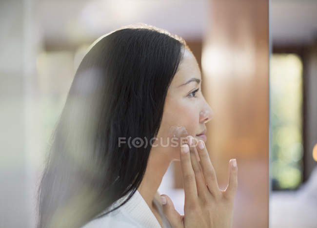Perfil mujer joven aplicando crema hidratante a la mejilla - foto de stock