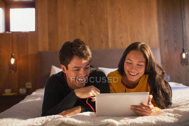 Felice giovane coppia con cuffie condividere tablet digitale sul letto — Foto stock