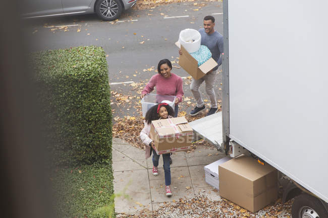 Family moving into new house, carrying belongings in driveway — Stock Photo