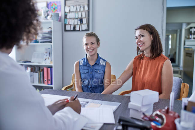 Smiling mother and daughter talking with daughter in clinic doctors office — Stock Photo