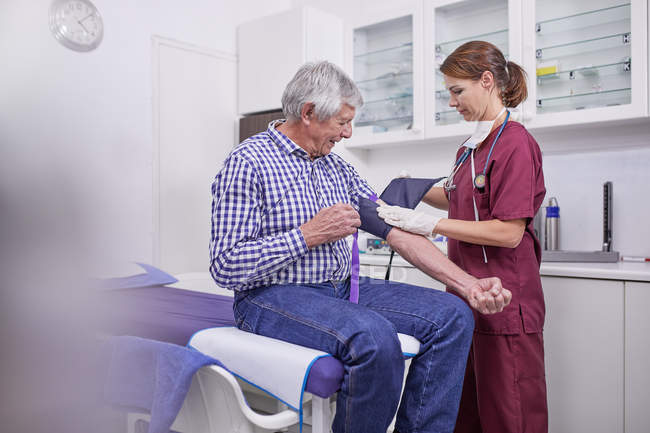 Female nurse checking blood pressure of senior male patient in clinic examination room — Stock Photo