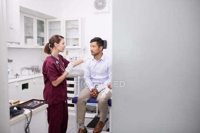 Female doctor talking with male patient in clinic examination room — Stock Photo